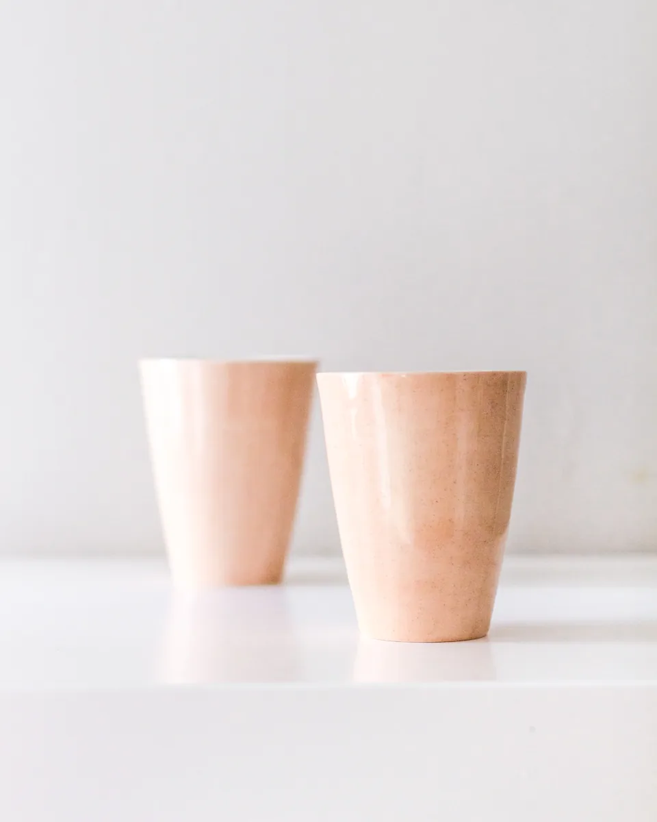 Dos vasos de cerámica color terracota, uno junto al otro, sobre una mesa blanca
