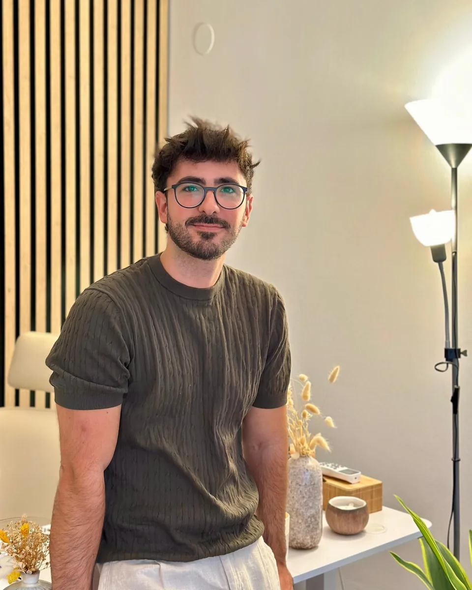 Rubén Lillo Moya, psicólogo general sanitario y sexólogo, sonríe a cámara de pie junto a una lámpara